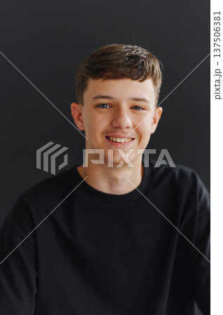 Happy young man smiles while sitting against a dark wall Happy young man smiles while sitting against a dark wall 137506381