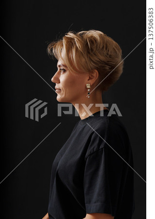 Woman with short hair and earrings stands against dark background 137506383