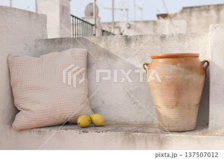 Mediterranean Terrace Still Life. Clay Pot, Linen Cushion, Fresh Lemons Fruit. Rustic Outdoor Balcony Scene. Sunlit Neutral Wall, Blurred Rooftop Background. Summer Home. Southern Europe Lifestyle 137507012