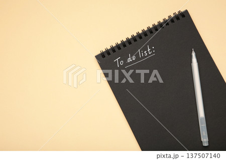 To do list on black notebook with white pen on beige background. To do list on black notebook with white pen on beige background. 137507140