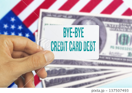 Human hand holding a plastic credit card with text bye bye credit card debt against a background of US dollar bills. Conceptual photography symbolizing financial freedom, paying off personal loans Human hand holding a plastic credit card with text bye bye credit card debt against a background of US dollar bills. Conceptual photography symbolizing financial freedom, paying off personal loans 137507493
