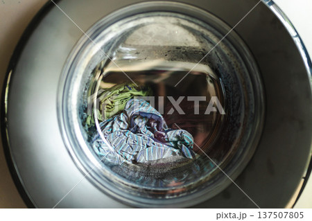 Laundry clothes inside washing machine drum seen through round glass door Laundry clothes inside washing machine drum seen through round glass door 137507805