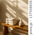 Morning light across spa bench, folded towels sit beside diffuser, soft shadows on wall, towels stacked neatly on warm wood, towels suggest cozy wellness, minimalist decor vibe, calm home bath theme 137508836