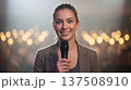 Smiling reporter holds microphone on stage. Microphone interview for election coverage, press conference, live broadcast concept, bokeh lights, news story, microphone closeup, media branding 137508910