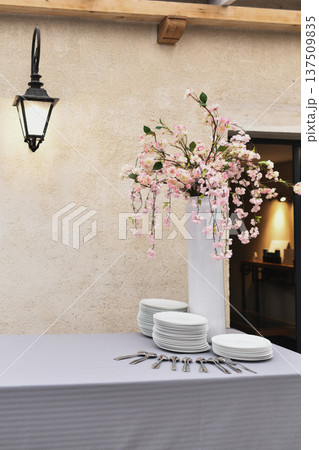 Outdoor wedding buffet table with plates and blooming pink centerpiece in a vase Outdoor wedding buffet table with plates and blooming pink centerpiece in a vase 137509835