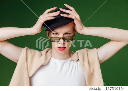 Young blond man with make up on his face and sunglasses. Man wearing fashionable white t-shirt and black cap. Man isolated on green background. Young blond man with make up on his face and sunglasses. Man wearing fashionable white t-shirt and black cap. Man isolated on green background. 137510194