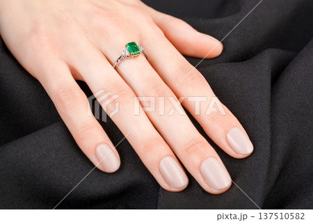 Beautiful female hand with gold ring with diamonds and emerald on gray background Beautiful female hand with gold ring with diamonds and emerald on gray background 137510582