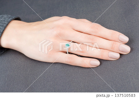 Beautiful female hand with gold ring with diamonds and emerald on gray background Beautiful female hand with gold ring with diamonds and emerald on gray background 137510583