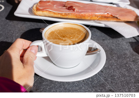 Woman drinking coffee with milk and eating tostada with ham in a cafe outside. Woman drinking coffee with milk and eating tostada with ham in a cafe outside. 137510703