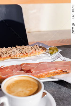 Coffee with milk and tostadas with tuna and ham. Spanish breakfast in a cafe outside. 137510706