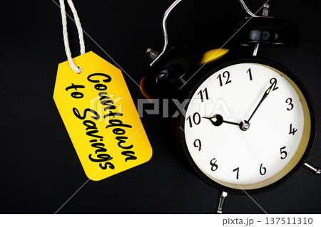 Price tag with message "Countdown to Savings" and alarm clock on black background 137511310