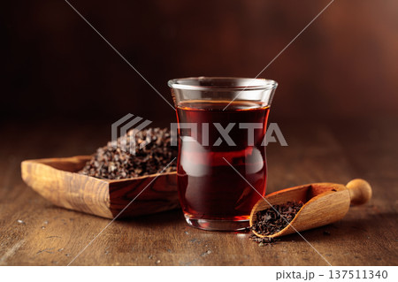 Glass transparent cup of black tea and dry tea in old wooden dish. 137511340