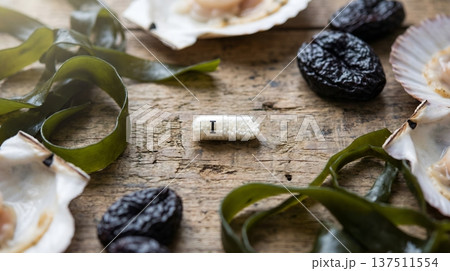 Iodine supplement capsule surrounded by natural food sources rich in iodine, scallops, seaweed, dried fruit, and nuts for thyroid health concepts 137511554