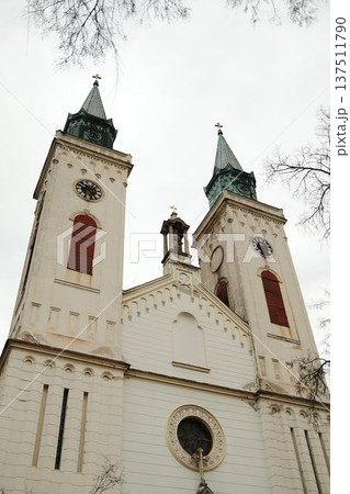 Twin church towers with clocks rising above winter trees in Sombor, Serbia. Symmetrical European landmark and cultural heritage concept Twin church towers with clocks rising above winter trees in Sombor, Serbia. Symmetrical European landmark and cultural heritage concept 137511790