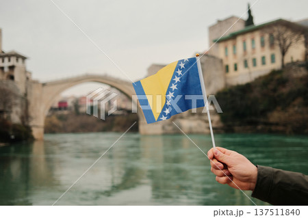 Hand holding Bosnia and Herzegovina flag in front of Stari Most bridge over Neretva river in Mostar. Symbol of national identity, history, travel and cultural heritage Hand holding Bosnia and Herzegovina flag in front of Stari Most bridge over Neretva river in Mostar. Symbol of national identity, history, travel and cultural heritage 137511840