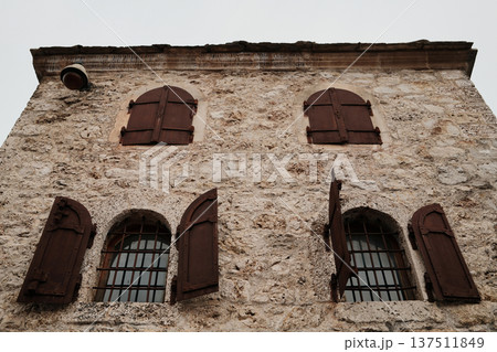 Facade of historic stone house in Mostar with wooden shutters and iron window bars. Traditional Balkan architecture showing preserved old town character Facade of historic stone house in Mostar with wooden shutters and iron window bars. Traditional Balkan architecture showing preserved old town character 137511849