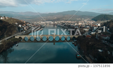Aerial view of the historic Mehmed Pasha Sokolovic Bridge crossing the Drina River in Visegrad, Bosnia and Herzegovina. Timeless Ottoman architecture meets calm river landscape Aerial view of the historic Mehmed Pasha Sokolovic Bridge crossing the Drina River in Visegrad, Bosnia and Herzegovina. Timeless Ottoman architecture meets calm river landscape 137511856