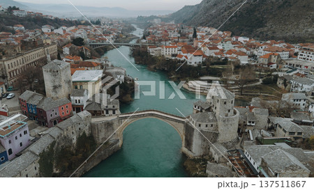Aerial view of the historic stone bridge over the Neretva River in Mostar, with old town architecture, turquoise water, and surrounding mountains under an overcast sky. Amazing Bosnia and Herzegovina Aerial view of the historic stone bridge over the Neretva River in Mostar, with old town architecture, turquoise water, and surrounding mountains under an overcast sky. Amazing Bosnia and Herzegovina 137511867
