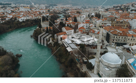 Aerial view of Mostar with turquoise Neretva River flowing through the historic old town. Stone mosque minarets and red roofs reflect the layered cultural heritage of Bosnia and Herzegovina Aerial view of Mostar with turquoise Neretva River flowing through the historic old town. Stone mosque minarets and red roofs reflect the layered cultural heritage of Bosnia and Herzegovina 137511873