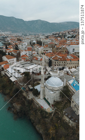 Aerial view of Mostar with turquoise Neretva River flowing through the historic old town. Stone mosque minarets and red roofs reflect the layered cultural heritage of Bosnia and Herzegovina Aerial view of Mostar with turquoise Neretva River flowing through the historic old town. Stone mosque minarets and red roofs reflect the layered cultural heritage of Bosnia and Herzegovina 137511874