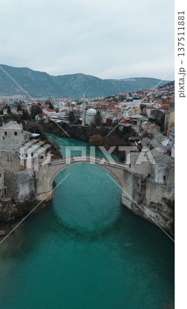 Aerial view of the historic stone bridge over the Neretva River in Mostar, with old town architecture, turquoise water, and surrounding mountains under an overcast sky. Amazing Bosnia and Herzegovina Aerial view of the historic stone bridge over the Neretva River in Mostar, with old town architecture, turquoise water, and surrounding mountains under an overcast sky. Amazing Bosnia and Herzegovina 137511881