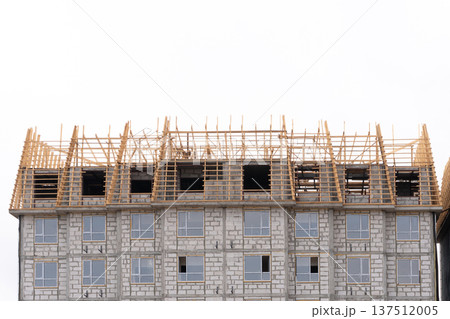 Wooden roof frame structure on top of an unfinished concrete building. Residential house construction site against white sky. Copy space 137512005