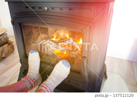 Feet in cozy socks on front of fire in wood stove in cold. Warm socks at wood stove in fire burns  137512120