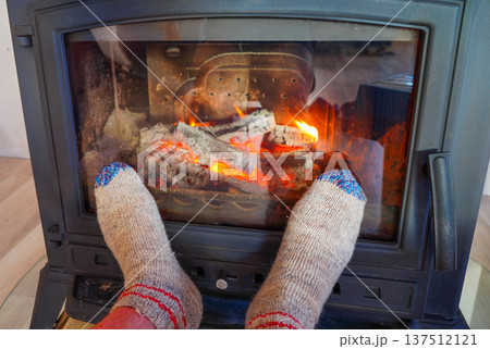 Feet in cozy socks on front of fire in wood stove in cold. Warm socks at wood stove in fire burns  137512121