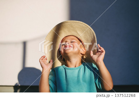 Smiling child wearing big straw hat in warm sunlight. 137512268
