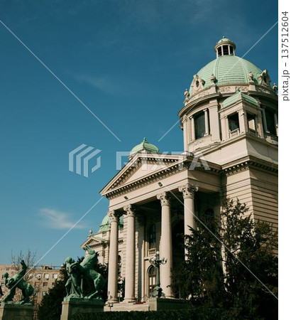 National Assembly building with classical columns and bronze sculptures in front of the entrance under a clear blue sky in Belgrade National Assembly building with classical columns and bronze sculptures in front of the entrance under a clear blue sky in Belgrade 137512604