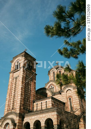 Saint Mark Church with striped brick facade and bell tower rising against a clear blue sky framed by pine branches in Belgrade Saint Mark Church with striped brick facade and bell tower rising against a clear blue sky framed by pine branches in Belgrade 137512609