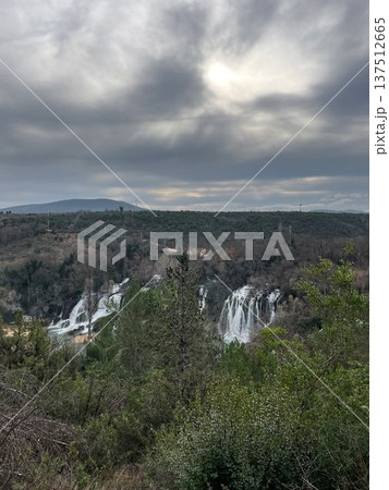 Panoramic view of Kravica Waterfall surrounded by forest and hills under dramatic cloudy sky. Scenic Balkan nature scene with multiple cascades and wild landscape Panoramic view of Kravica Waterfall surrounded by forest and hills under dramatic cloudy sky. Scenic Balkan nature scene with multiple cascades and wild landscape 137512665