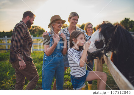 Little girl with mother feeding horse outdoors at community farm. 137512846