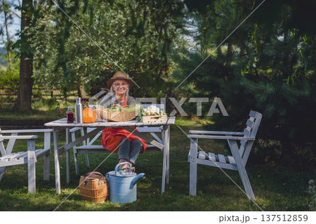 Happy senior female farmer sitting with homegrown vegetables and resting. Happy senior female farmer sitting with homegrown vegetables and resting. 137512859