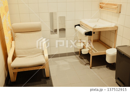 Clean baby care room with a changing table, chair, paper dispenser, and tiled walls, designed for comfort and hygiene in public spaces Clean baby care room with a changing table, chair, paper dispenser, and tiled walls, designed for comfort and hygiene in public spaces 137512915