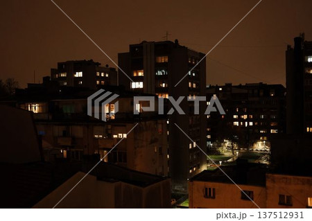 Night view of residential apartment buildings with glowing windows under an overcast sky. Urban neighborhood atmosphere with warm city lights, quiet evening mood and dense housing skyline 137512931