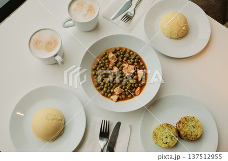 Top view of a lunch table with green pea stew and chicken, mashed potatoes, vegetable patties and coffee cups. Balanced home style meal concept, simple cafeteria food 137512955