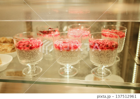 Chia seed pudding served in glass cups with raspberry topping inside a cafe display case. Healthy dessert concept, modern cafe menu, fresh sweets presentation Chia seed pudding served in glass cups with raspberry topping inside a cafe display case. Healthy dessert concept, modern cafe menu, fresh sweets presentation 137512961