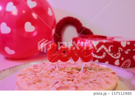 Romantic cake topped with almond flakes and red love candle, surrounded by heart decorations and gift box. Festive dessert concept for Valentine celebration and romantic moments 137512980