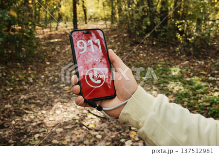 Hand holding a smartphone showing a 911 emergency call screen in a forest path. Concept of danger, urgent help request, outdoor accident risk and emergency communication in nature Hand holding a smartphone showing a 911 emergency call screen in a forest path. Concept of danger, urgent help request, outdoor accident risk and emergency communication in nature 137512981