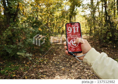 Hand holding a smartphone showing a 911 emergency call screen in a forest path. Concept of danger, urgent help request, outdoor accident risk and emergency communication in nature Hand holding a smartphone showing a 911 emergency call screen in a forest path. Concept of danger, urgent help request, outdoor accident risk and emergency communication in nature 137512982