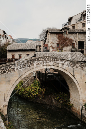 Kriva Cuprija stone bridge in Mostar crossing a shallow river, surrounded by historic houses and old town architecture. Medieval Balkan landmark reflecting cultural heritage and calm urban atmosphere Kriva Cuprija stone bridge in Mostar crossing a shallow river, surrounded by historic houses and old town architecture. Medieval Balkan landmark reflecting cultural heritage and calm urban atmosphere 137512986