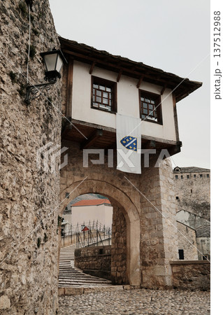 Stone gate and arched passage in Mostar old town with traditional architecture and cobblestone street. Historic Balkan urban scene reflecting cultural heritage 137512988