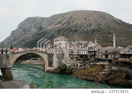 Historic stone bridge and old town of Mostar spanning the turquoise Neretva River, surrounded by traditional buildings and mountains. Iconic Balkan landmark representing culture, heritage, and travel Historic stone bridge and old town of Mostar spanning the turquoise Neretva River, surrounded by traditional buildings and mountains. Iconic Balkan landmark representing culture, heritage, and travel 137513031