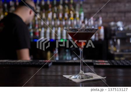 A dark alcoholic cocktail in a martini glass served on a napkin on a bar counter A dark alcoholic cocktail in a martini glass served on a napkin on a bar counter 137513127