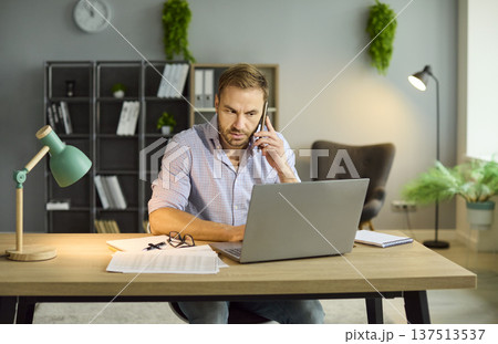 Business man talking by phone working on workplace with laptop in office. Business man talking by phone working on workplace with laptop in office. 137513537