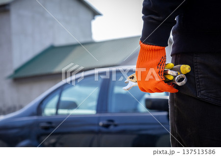 A man stands in a workshop area holding a tool in his hand while a car is parked nearby. It is a clear day and he seems ready to work 137513586
