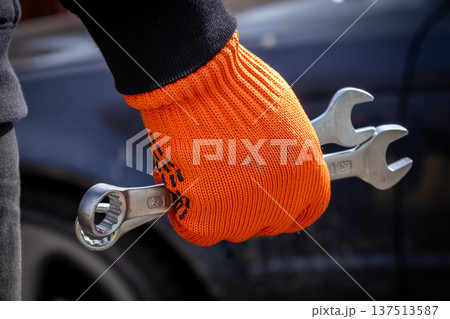 A man stands ready to fix a car with tools in hand inside a garage during the day A man stands ready to fix a car with tools in hand inside a garage during the day 137513587