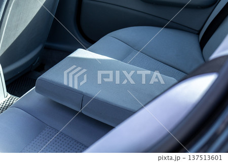 A back seat area is shown with comfortable car seats. A center armrest is placed on one of the seats during daytime A back seat area is shown with comfortable car seats. A center armrest is placed on one of the seats during daytime 137513601
