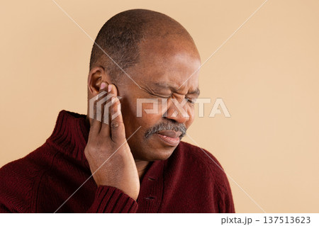 Mature black man touching ear with uncomfortable expression on beige studio background 137513623